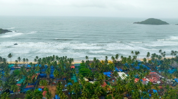 Aerial view of Palolem Beach with lush palm trees colorful beach huts and waves rolling onto the sandy shore in Canacona Goa India.