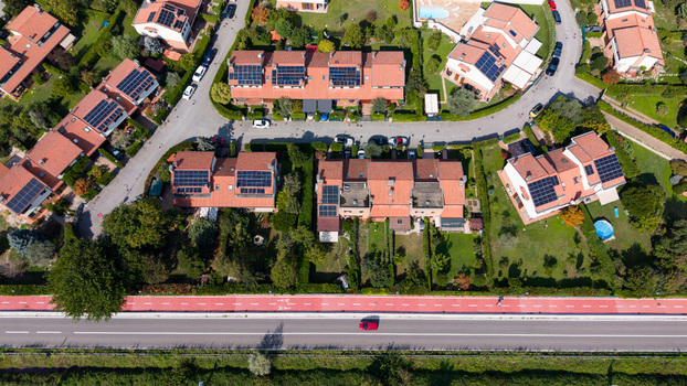 Aerial view of modern residential houses with solar panels on red tiled roofs lush green gardens and a red bicycle path along a road in Milan Lombardy Italy. Aerial view of modern residential houses with solar panels on red tiled roofs lush green gardens and a red bicycle path along a road in Milan Lombardy Italy.
