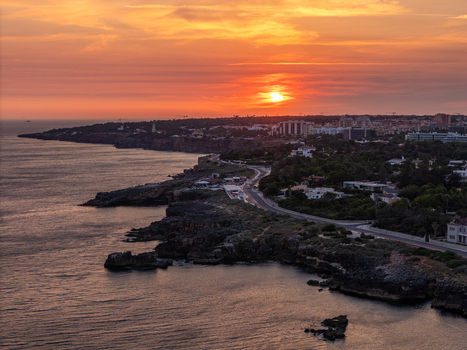 Aerial view of the rugged coastline at sunset with golden light reflecting on the Atlantic Ocean coastal roads and residential buildings in Cascais Lisboa Portugal. Aerial view of the rugged coastline at sunset with golden light reflecting on the Atlantic Ocean coastal roads and residential buildings in Cascais Lisboa Portugal.