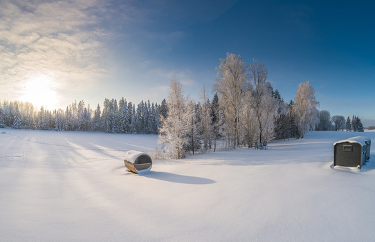 Aerial view of a barrel sauna in a snow covered field surrounded by frost covered trees under a bright winter sun in Latvia. Aerial view of a barrel sauna in a snow covered field surrounded by frost covered trees under a bright winter sun in Latvia.