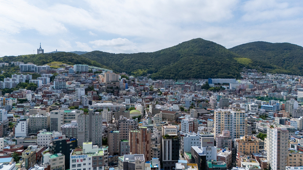 Aerial view of the dense urban landscape of Busan featuring high rise residential buildings commercial structures and lush green hills under a bright sky in Busan Busan South Korea. Aerial view of the dense urban landscape of Busan featuring high rise residential buildings commercial structures and lush green hills under a bright sky in Busan Busan South Korea.