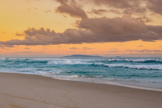 View of the sandy beach and turquoise ocean waves at sunset with a distant island on the horizon at Sandpatch Western Australia Australia. View of the sandy beach and turquoise ocean waves at sunset with a distant island on the horizon at Sandpatch Western Australia Australia.