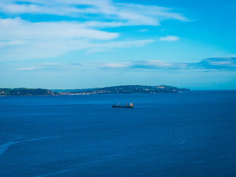 Aerial view of a cargo ship sailing on the calm blue waters of the Irish Sea near the coastline with rolling green hills Bangor Northern Ireland United Kingdom.