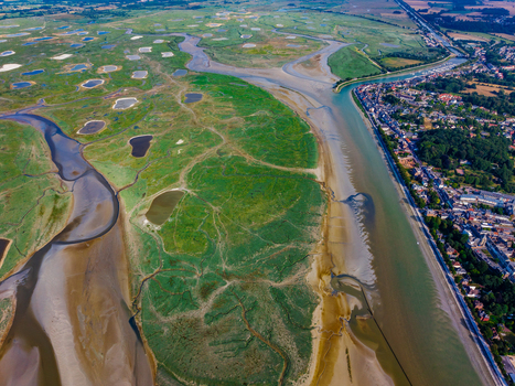 Aerial view of the Baie de Somme featuring winding tidal channels lush green salt marshes and small water pools adjacent to the coastal town of Saint Valery sur Somme Hauts de France France. Aerial view of the Baie de Somme featuring winding tidal channels lush green salt marshes and small water pools adjacent to the coastal town of Saint Valery sur Somme Hauts de France France.