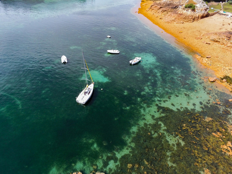 Aerial view of boats anchored in the clear turquoise waters off the coast of Brehat with rocky shorelines and sandy beaches in Ile de Brehat Brittany France.