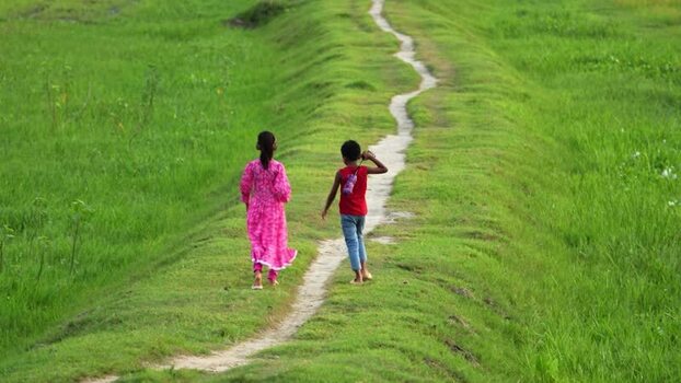 View of two children walking on a path in green fields Bangladesh.
