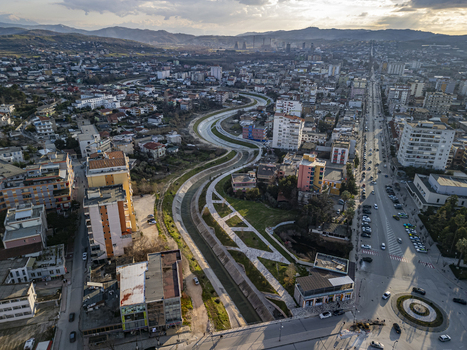 Aerial view of the Gjanica River winding through the urban landscape of Fier featuring modern buildings paved roads a roundabout and surrounding hills in Fier Fier County Albania. Aerial view of the Gjanica River winding through the urban landscape of Fier featuring modern buildings paved roads a roundabout and surrounding hills in Fier Fier County Albania.