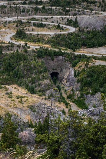 View of the tunnel entrance at the Complejo hidroelectrico Futaleufu with a winding road leading through the rocky forested landscape in Futaleufu Chubut Argentina. View of the tunnel entrance at the Complejo hidroelectrico Futaleufu with a winding road leading through the rocky forested landscape in Futaleufu Chubut Argentina.
