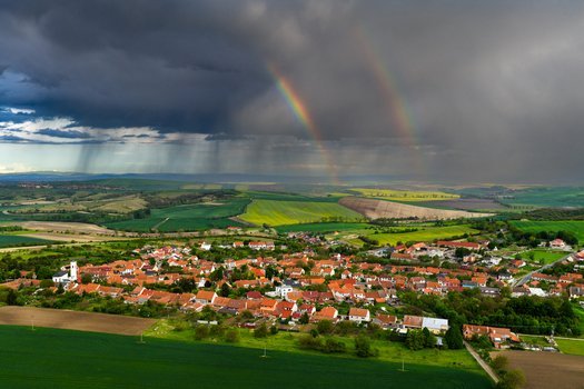 Aerial view of Nasedlovice village with red tiled rooftops surrounded by agricultural fields under a dramatic stormy sky with a double rainbow in Nasedlovice South Moravian Region Czechia.