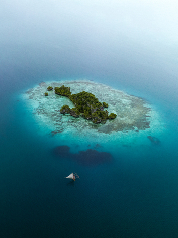 Aerial view of a lush green islet surrounded by vibrant turquoise waters and a passing sailboat Pine Island L Île des Pins New Caledonia. Aerial view of a lush green islet surrounded by vibrant turquoise waters and a passing sailboat Pine Island L Île des Pins New Caledonia.