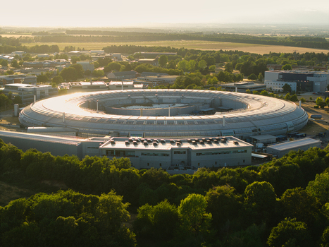 Aerial view of Diamond Light Source a circular synchrotron facility surrounded by greenery and industrial buildings under golden hour light in Didcot England United Kingdom.