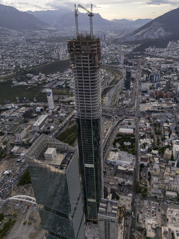 Aerial view of the Rise Tower under construction with cranes on top surrounded by the urban skyline city streets and mountains in Monterrey Nuevo Leon Mexico. Aerial view of the Rise Tower under construction with cranes on top surrounded by the urban skyline city streets and mountains in Monterrey Nuevo Leon Mexico.
