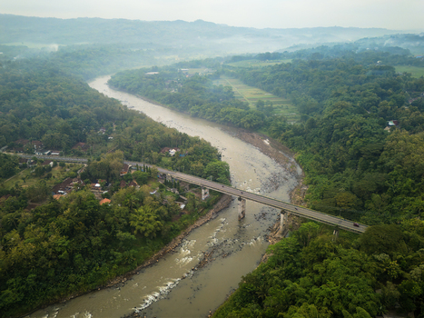 Aerial view of Kreo bridge spanning a wide river surrounded by lush tropical forests and rural landscapes in Kalibawang Special Region of Yogyakarta Indonesia.