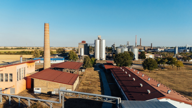 Aerial view of an industrial facility featuring a tall brick chimney metal grain silos and low rise buildings with red roofs in Sremska Mitrovica Vojvodina Serbia. Aerial view of an industrial facility featuring a tall brick chimney metal grain silos and low rise buildings with red roofs in Sremska Mitrovica Vojvodina Serbia.