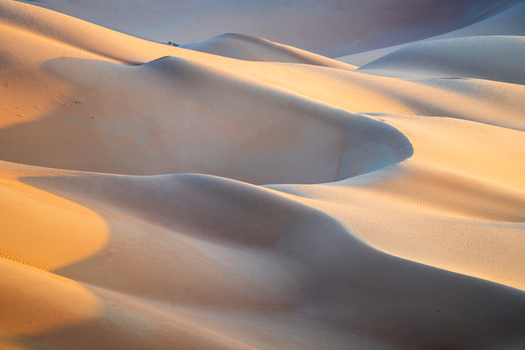 View of Eastern Sands featuring rolling sand dunes with soft golden light and deep shadows at sunset Oman. View of Eastern Sands featuring rolling sand dunes with soft golden light and deep shadows at sunset Oman.