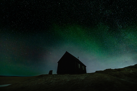 View of a solitary church silhouetted against a vibrant aurora borealis and a starry night sky Krysuvikurkirkja Hafnarfjardarkaupstadur Iceland.