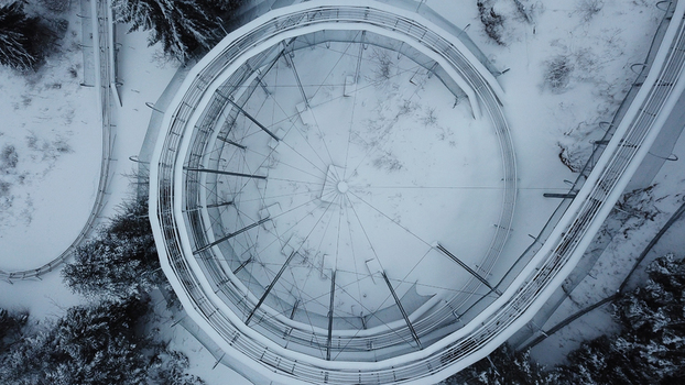 Aerial view of the Col de la Faucille summer sledge track covered in snow featuring a circular metal structure surrounded by snow covered pine trees in Gex Auvergne Rhone Alpes France. Aerial view of the Col de la Faucille summer sledge track covered in snow featuring a circular metal structure surrounded by snow covered pine trees in Gex Auvergne Rhone Alpes France.
