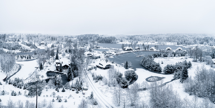 Aerial view of a snow covered landscape in Latvia featuring a frozen lake dense pine forests and wooden cabins under a cloudy winter sky in Latvia. Aerial view of a snow covered landscape in Latvia featuring a frozen lake dense pine forests and wooden cabins under a cloudy winter sky in Latvia.