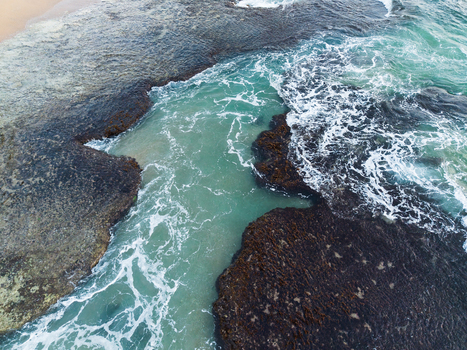 Aerial view of the rocky coastline with turquoise water and white foam crashing against dark reef formations in Galle Southern Province Sri Lanka. Aerial view of the rocky coastline with turquoise water and white foam crashing against dark reef formations in Galle Southern Province Sri Lanka.