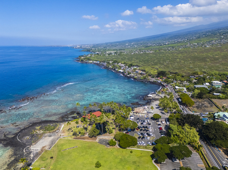 Aerial view of Kahalu u Beach Park featuring a vibrant coral reef black lava shoreline and lush palm trees along the coast in Kailua Kona Hawaii United States. Aerial view of Kahalu u Beach Park featuring a vibrant coral reef black lava shoreline and lush palm trees along the coast in Kailua Kona Hawaii United States.