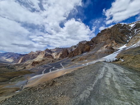 View of Penzi La road winding through the rugged Himalayan mountains with snow patches and rocky slopes under a blue sky in Zanskar Ladakh India.