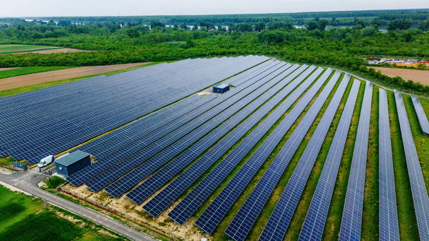 Aerial view of a large solar farm with rows of blue photovoltaic panels surrounded by lush green forests and a river in the background Sabac Vojvodina Serbia.