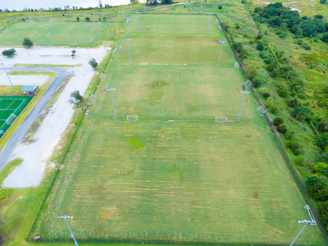 Aerial view of nCino Sports Park featuring multiple green soccer fields with floodlights and surrounding vegetation in Wilmington North Carolina United States. Aerial view of nCino Sports Park featuring multiple green soccer fields with floodlights and surrounding vegetation in Wilmington North Carolina United States.