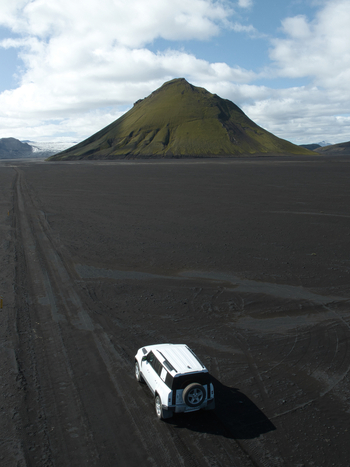 Aerial view of Maelifell volcano with moss covered slopes rising from a black volcanic sand desert with a white off road vehicle on a dirt track Kirkjubaejarklaustur Skaftarhreppur Iceland. Aerial view of Maelifell volcano with moss covered slopes rising from a black volcanic sand desert with a white off road vehicle on a dirt track Kirkjubaejarklaustur Skaftarhreppur Iceland.