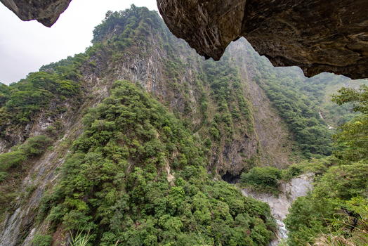 View of Taroko National Park featuring steep lush forested mountain slopes viewed from a rocky cave overhang in Xiulin Township Hualien County Taiwan.