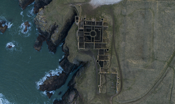 Aerial view of the historic ruins of Slains Castle perched on rugged cliffs overlooking the dark North Sea waves Cruden Bay Scotland United Kingdom. Aerial view of the historic ruins of Slains Castle perched on rugged cliffs overlooking the dark North Sea waves Cruden Bay Scotland United Kingdom.