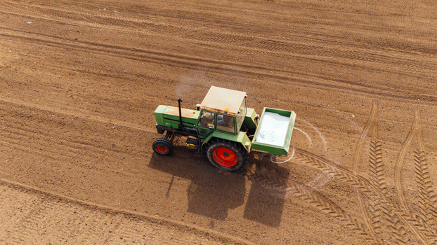 Aerial view of a green tractor spreading fertilizer across the dark soil of a farm field leaving white trails in its wake Sremska Mitrovica Vojvodina Serbia. Aerial view of a green tractor spreading fertilizer across the dark soil of a farm field leaving white trails in its wake Sremska Mitrovica Vojvodina Serbia.