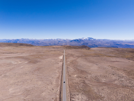 Aerial view of the Mirador de los Andes with a long straight road cutting through the arid landscape and snow capped mountains in the distance in Caylloma Arequipa Peru.