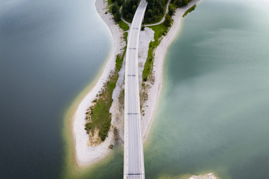 Aerial view of a stark white bridge cutting through the contrasting dark and light blues of the Sylvensteinsee Sylvensteinspeicher Bayern Germany. Aerial view of a stark white bridge cutting through the contrasting dark and light blues of the Sylvensteinsee Sylvensteinspeicher Bayern Germany.