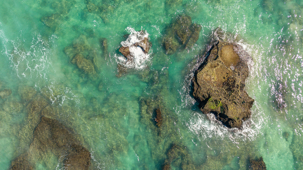 Aerial view of the rocky coastline of Hartenbos with turquoise ocean water and white waves crashing against dark reefs in Mossel Bay Western Cape South Africa. Aerial view of the rocky coastline of Hartenbos with turquoise ocean water and white waves crashing against dark reefs in Mossel Bay Western Cape South Africa.