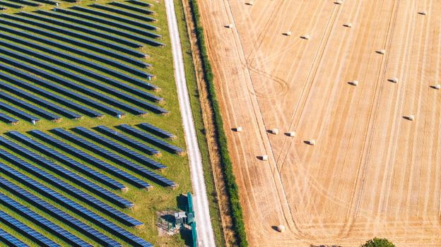 Aerial view of a solar farm with rows of photovoltaic panels adjacent to a harvested field with scattered hay bales in Dorset England United Kingdom.