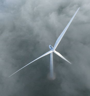 Aerial view of a modern wind turbine emerging from a thick layer of white fog and clouds in Netherlands. Aerial view of a modern wind turbine emerging from a thick layer of white fog and clouds in Netherlands.