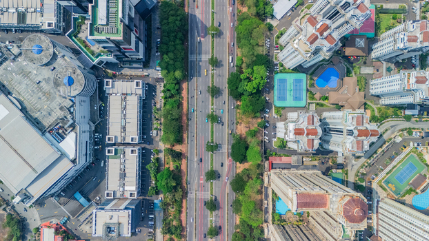 Aerial view of a busy urban street flanked by high rise apartment complexes lush green trees and tennis courts in Jakarta Indonesia. Aerial view of a busy urban street flanked by high rise apartment complexes lush green trees and tennis courts in Jakarta Indonesia.