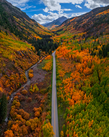 Aerial view of Maroon Bells surrounded by vibrant autumn foliage a winding road cutting through the valley and a mountain stream in Pitkin County Colorado United States.