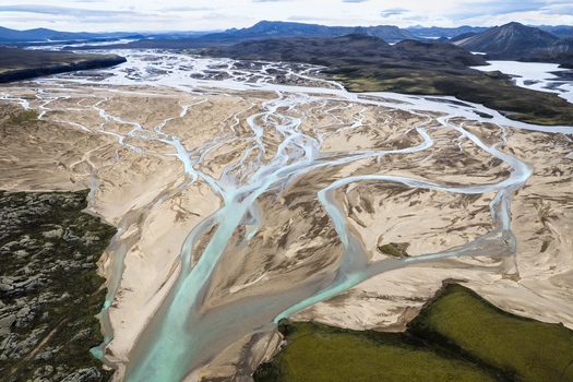 Aerial view of the intricate braided glacial river system with turquoise water flowing through sandy volcanic plains and mountains near F208 Icelandic Highlands Iceland. Aerial view of the intricate braided glacial river system with turquoise water flowing through sandy volcanic plains and mountains near F208 Icelandic Highlands Iceland.