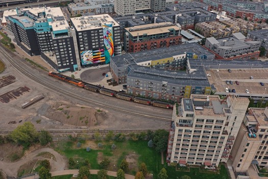 Aerial view of a freight train traveling along the tracks through a modern urban neighborhood with apartment complexes a colorful mural and green spaces in Denver Colorado United States. Aerial view of a freight train traveling along the tracks through a modern urban neighborhood with apartment complexes a colorful mural and green spaces in Denver Colorado United States.