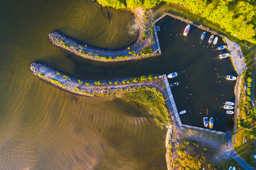 Aerial view of the small harbor at Vanersnas with several boats moored at the docks surrounded by lush green trees and calm water in Vanersnas Vastra Gotalands lan Sweden. Aerial view of the small harbor at Vanersnas with several boats moored at the docks surrounded by lush green trees and calm water in Vanersnas Vastra Gotalands lan Sweden.