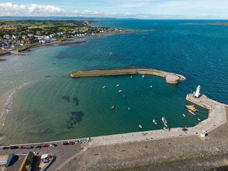 Aerial view of Donaghadee Harbour with its iconic lighthouse small boats moored in the calm bay and the coastal town in the background Donaghadee Northern Ireland United Kingdom. Aerial view of Donaghadee Harbour with its iconic lighthouse small boats moored in the calm bay and the coastal town in the background Donaghadee Northern Ireland United Kingdom.