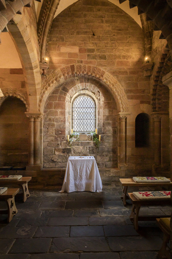 View of the historic interior of a stone chapel featuring a central altar arched window and wooden benches in Newcastle upon Tyne England United Kingdom. View of the historic interior of a stone chapel featuring a central altar arched window and wooden benches in Newcastle upon Tyne England United Kingdom.