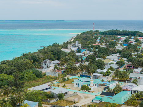 Aerial view of a tranquil island village fringed by turquoise waters where homes nestle amongst lush greenery under the equatorial sun Vashafaru Island Maldives. Aerial view of a tranquil island village fringed by turquoise waters where homes nestle amongst lush greenery under the equatorial sun Vashafaru Island Maldives.