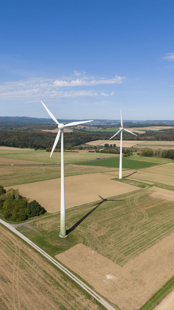 Aerial view of Windpark Eppenrod featuring two large wind turbines standing in agricultural fields under a clear blue sky in Eppenrod Rheinland Pfalz Germany.