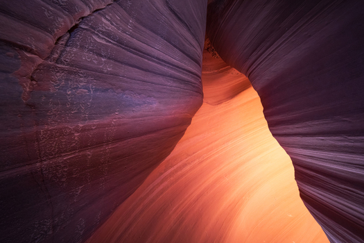 View of smooth sculpted sandstone walls casting shadows leading to a bright orange glow within the canyon s depths Escalante Utah United States.