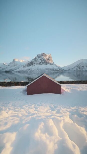 View of a red boathouse and snow capped mountains Norway.