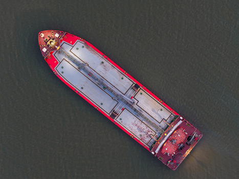 Aerial view of a cargo ship navigating the Mahakam River with a red hull and grey deck in Samarinda East Kalimantan Indonesia. Aerial view of a cargo ship navigating the Mahakam River with a red hull and grey deck in Samarinda East Kalimantan Indonesia.