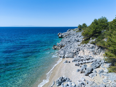 Aerial view of a secluded pebble beach and rugged rocky cliffs meeting the turquoise Aegean Sea under a clear blue sky Pallini Greece.