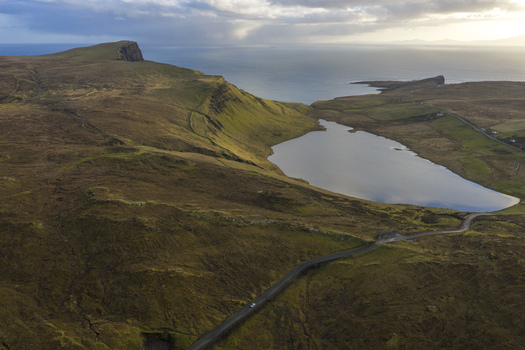 Aerial view of Loch Mor surrounded by rugged green hills and a winding road near the coastline Isle of Skye Scotland United Kingdom.